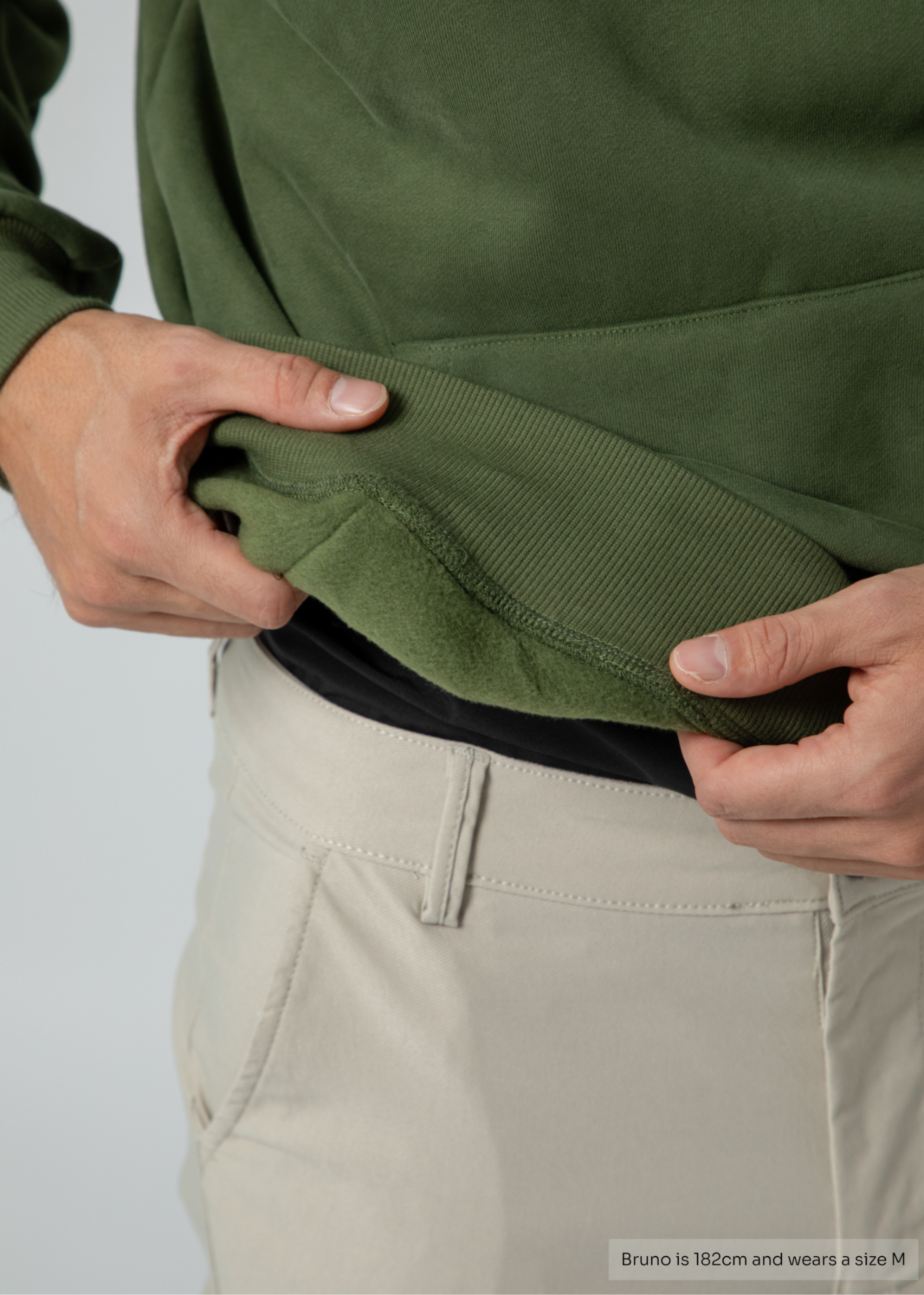 Person wearing a green jacket and beige pants with a plain background