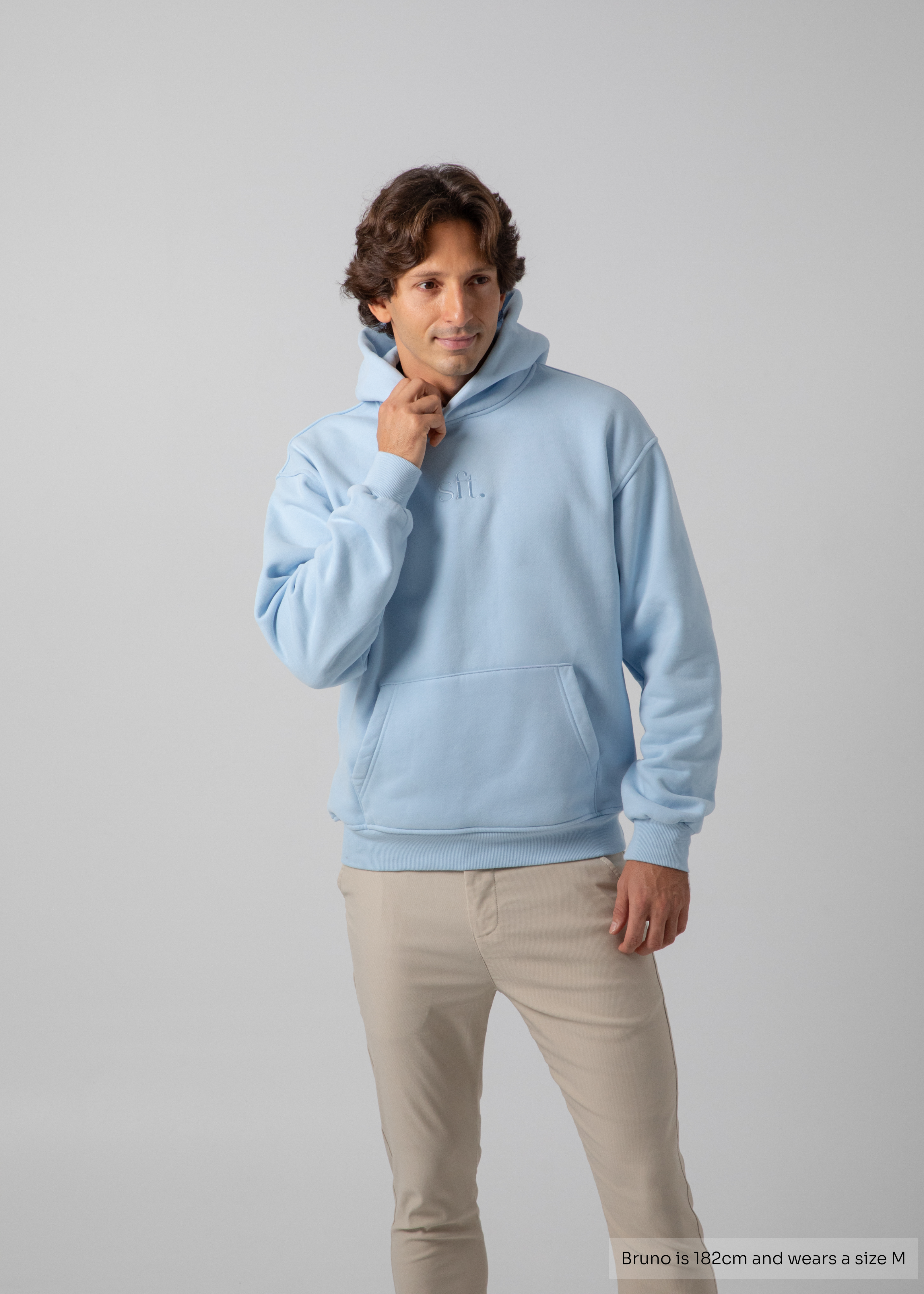 Man wearing a light blue hoodie and beige pants on a gray background