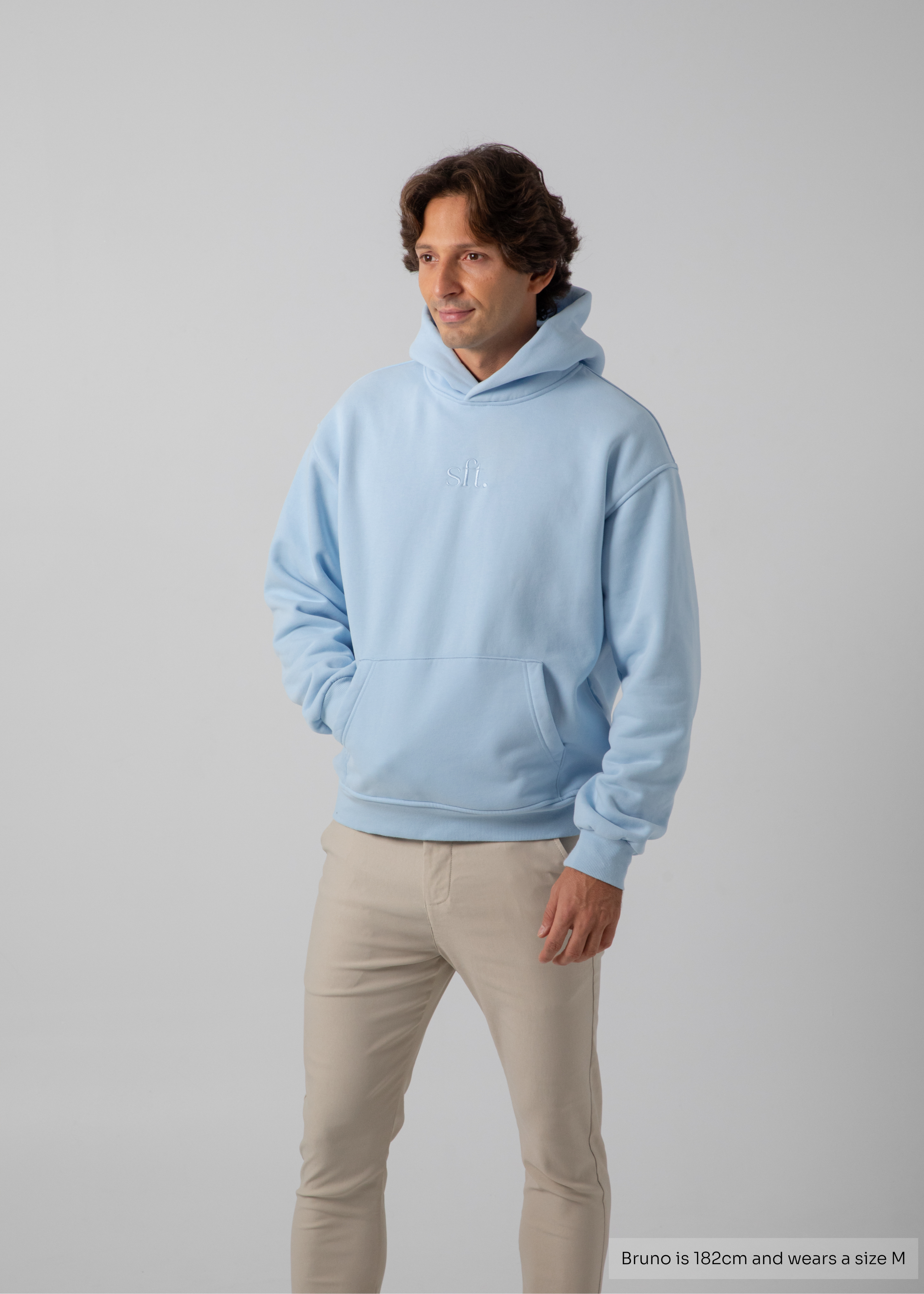 Man wearing a light blue hoodie and beige pants on a gray background