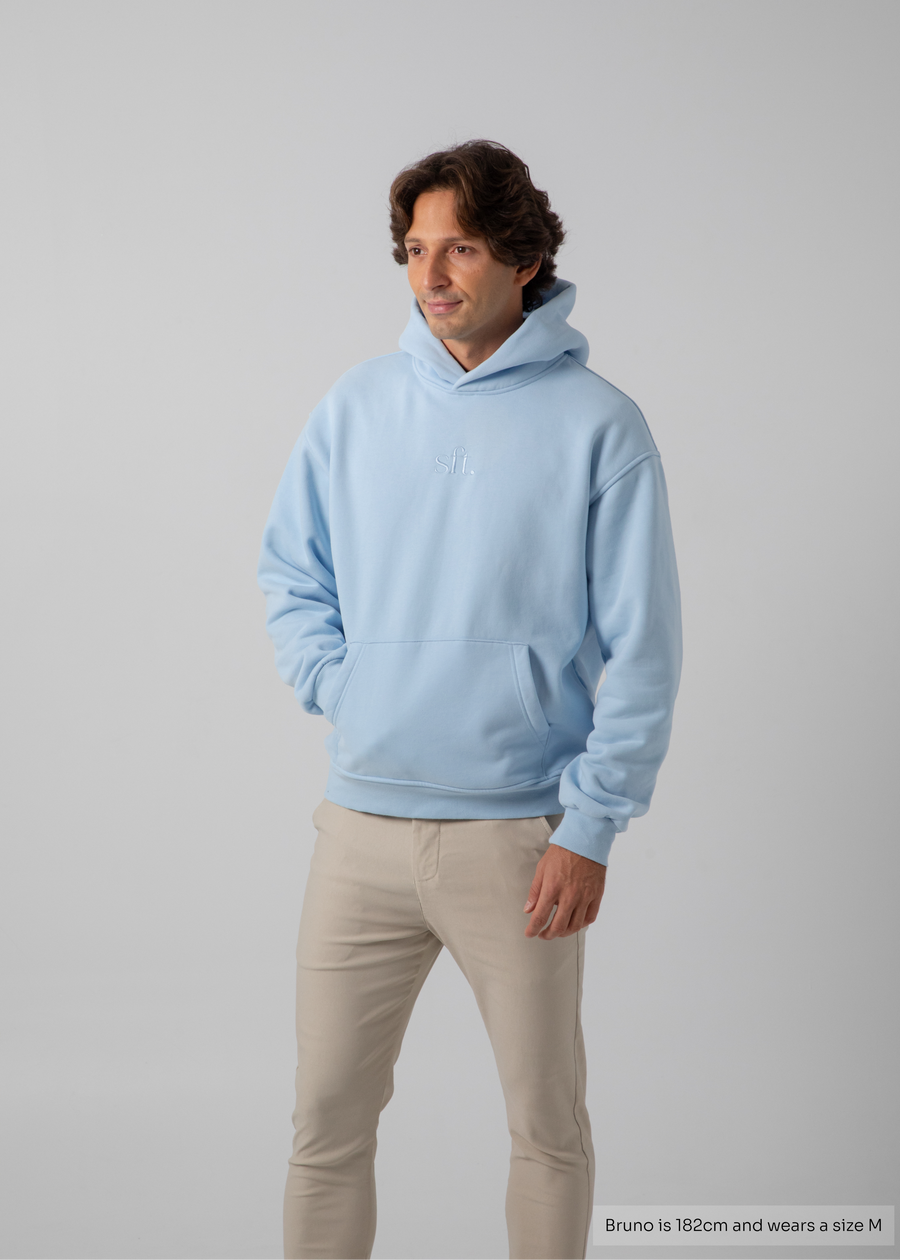 Man wearing a light blue hoodie and beige pants on a gray background